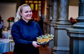 A staff member smiling to the camera while holding a tray of canapés.