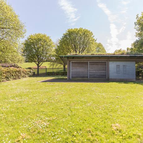 A single level wooden building in a grassy landscape surrounded by trees.
