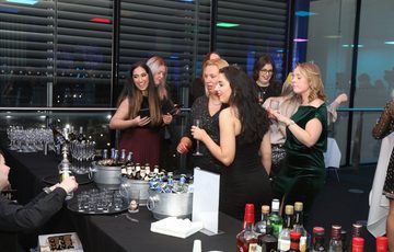 A group of people standing at a bar table full of drinks.
